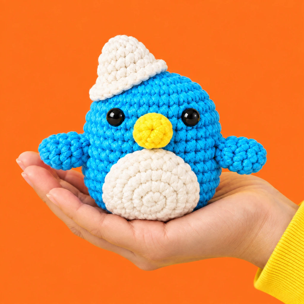 Colin — Pingouin bleu à bonnet blanc au crochet — présentation en main.